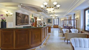 A spacious hotel lobby with a wooden reception desk, comfortable seating, and a large chandelier. - Tmark Hotel Vaticano (Rome)