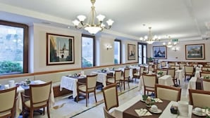 A dining area with multiple tables and chairs, large windows, and artwork on the walls. - Tmark Hotel Vaticano (Rome)