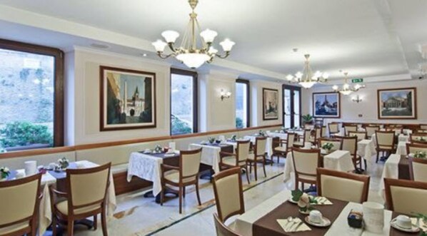 A dining area with multiple tables and chairs, large windows, and artwork on the walls. - Tmark Hotel Vaticano (Rome)