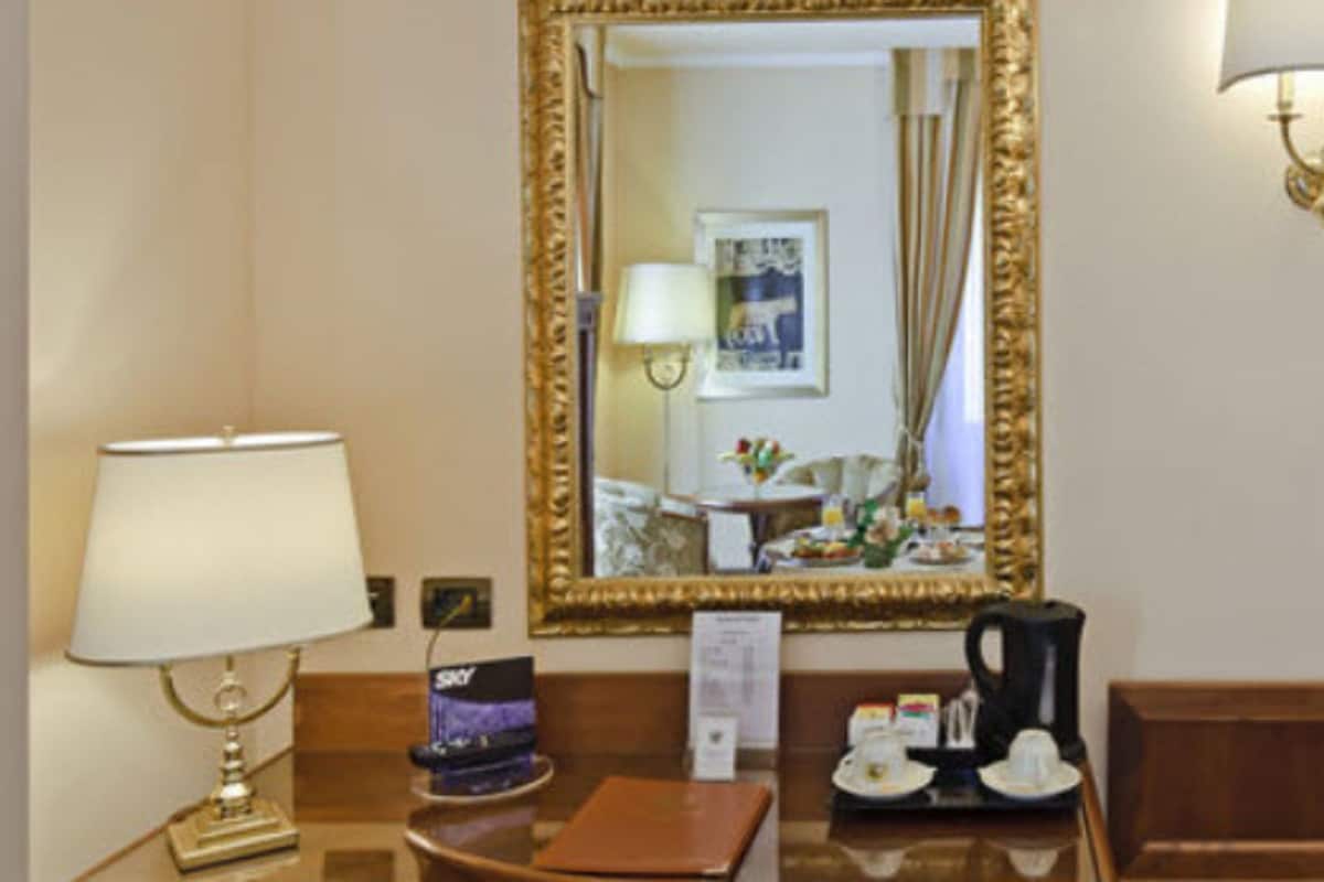 A hotel room with a wooden desk, a mirror, a lamp, a coffee maker, and a tray with a cup and saucer.