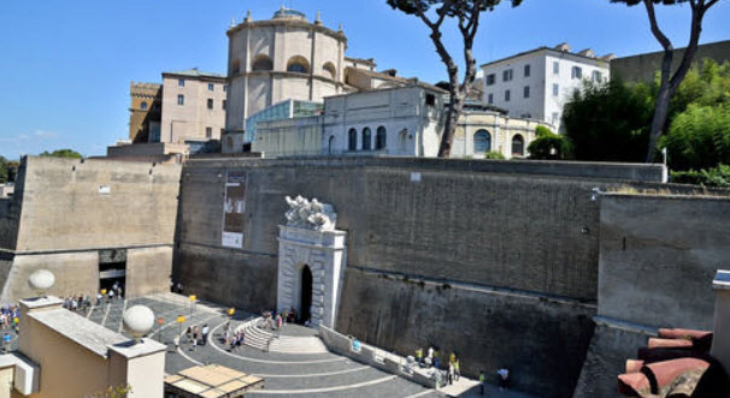 A historical building with a central courtyard, a prominent archway, and a dome structure in the background.