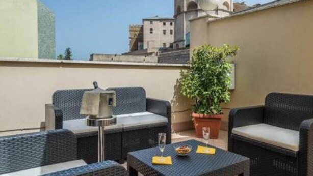 A rooftop terrace with wicker furniture, a table with a glass, and a potted plant. - Tmark Hotel Vaticano (Rome)