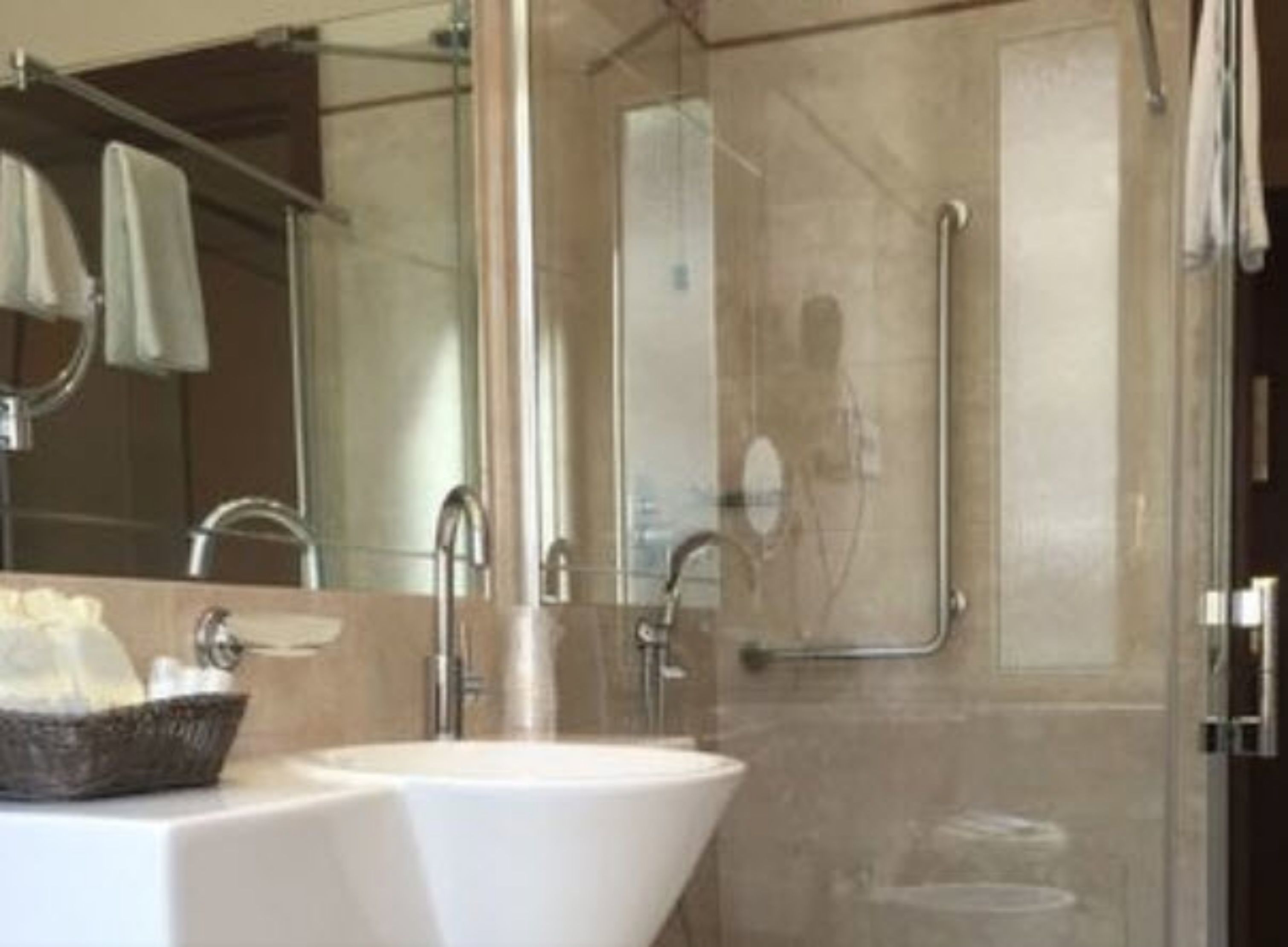 Ein modernes Badezimmer mit einem weißen Waschbecken, einer Duschkabine aus Glas und einer Handstange.