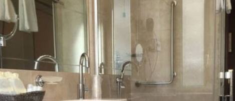 A modern bathroom with a white sink, a glass shower enclosure, and a handrail.