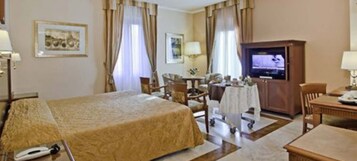 A hotel room with a large bed, a desk with a television, a chair, and a table with a lamp.