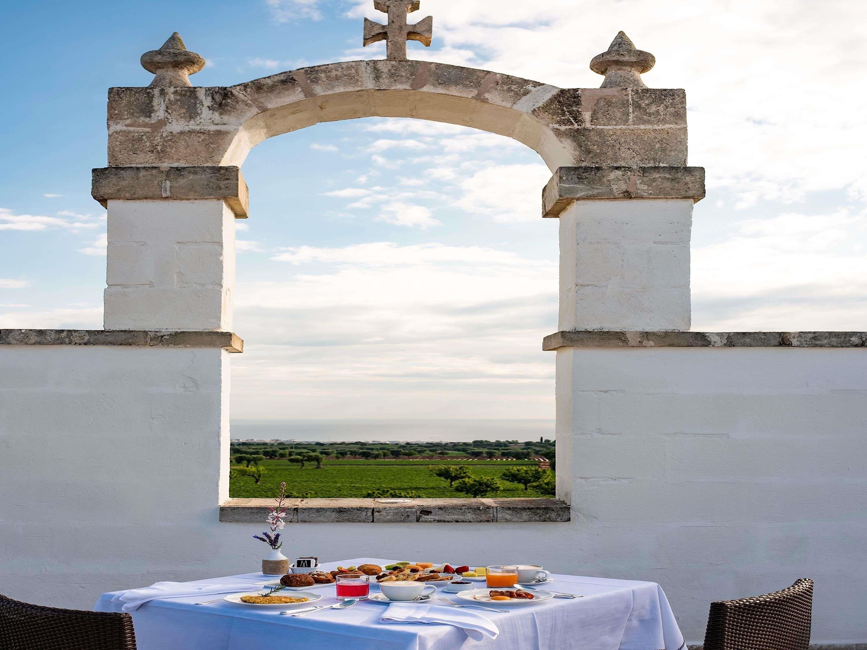 Une table dressée avec des aliments pour le petit-déjeuner, et une vue sur un paysage verdoyant à travers une arche.