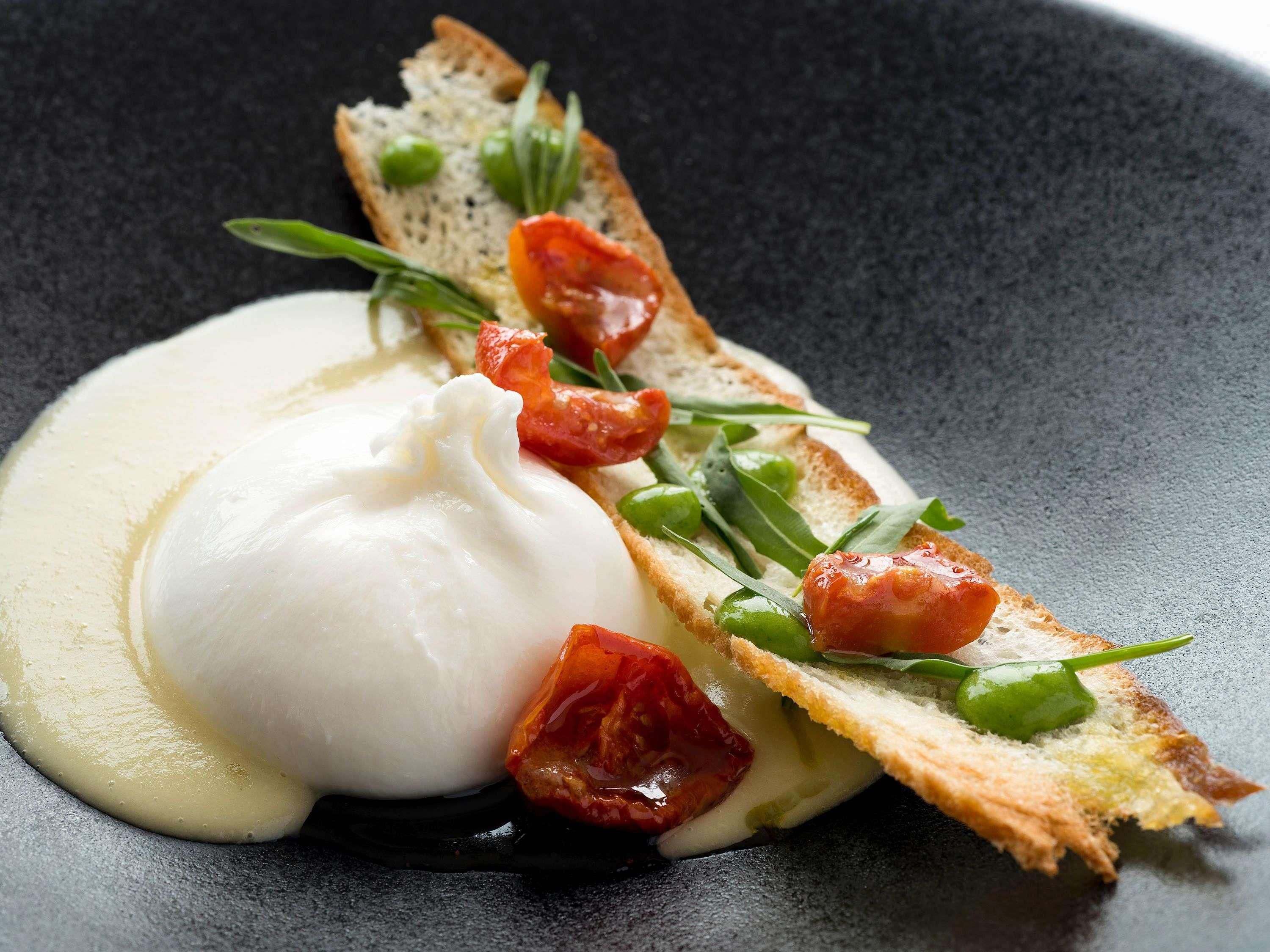 Un piatto con uovo in camicia, pomodoro e verdure su una fetta di pane.