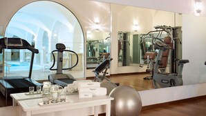 Een sportschool met trainingsapparatuur, een grote spiegel en een tafel met handdoeken en glazen.
