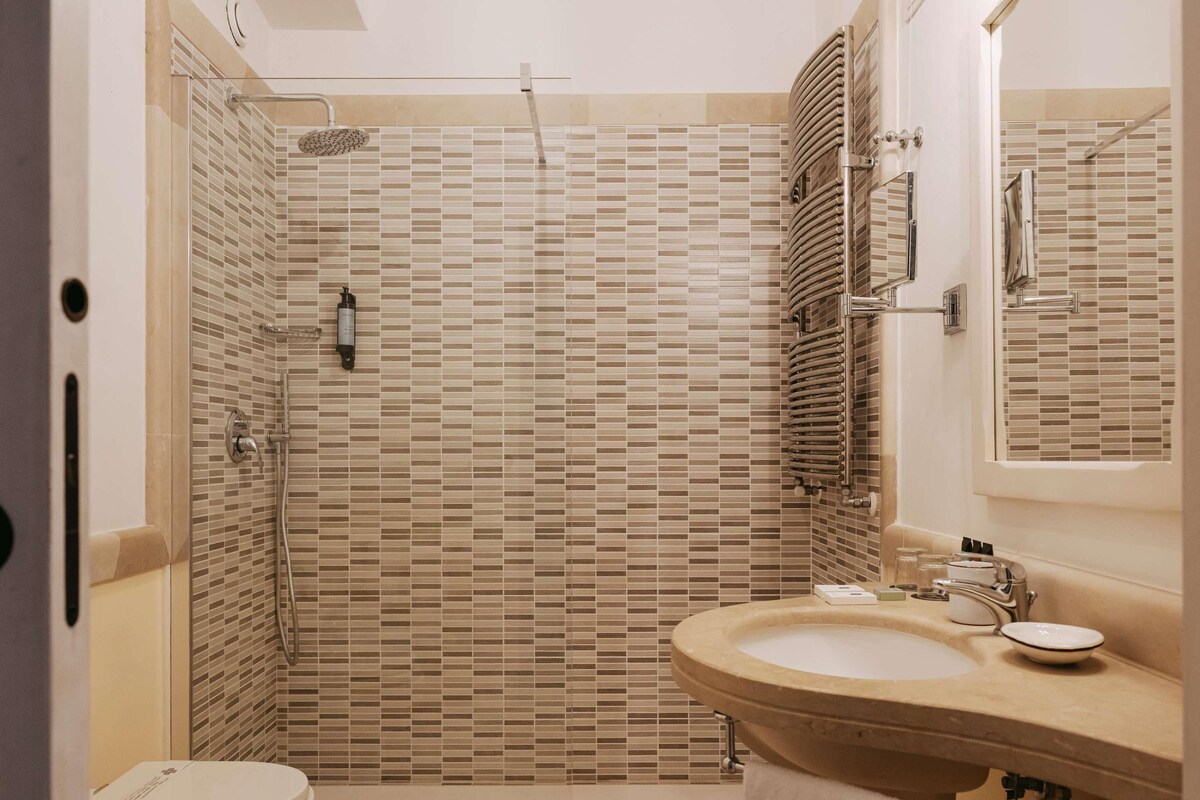 Une salle de bain avec une douche carrelée, des toilettes et un lavabo avec un miroir.