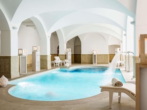 A swimming pool with a water fountain, lounge chairs, and a high arched ceiling.