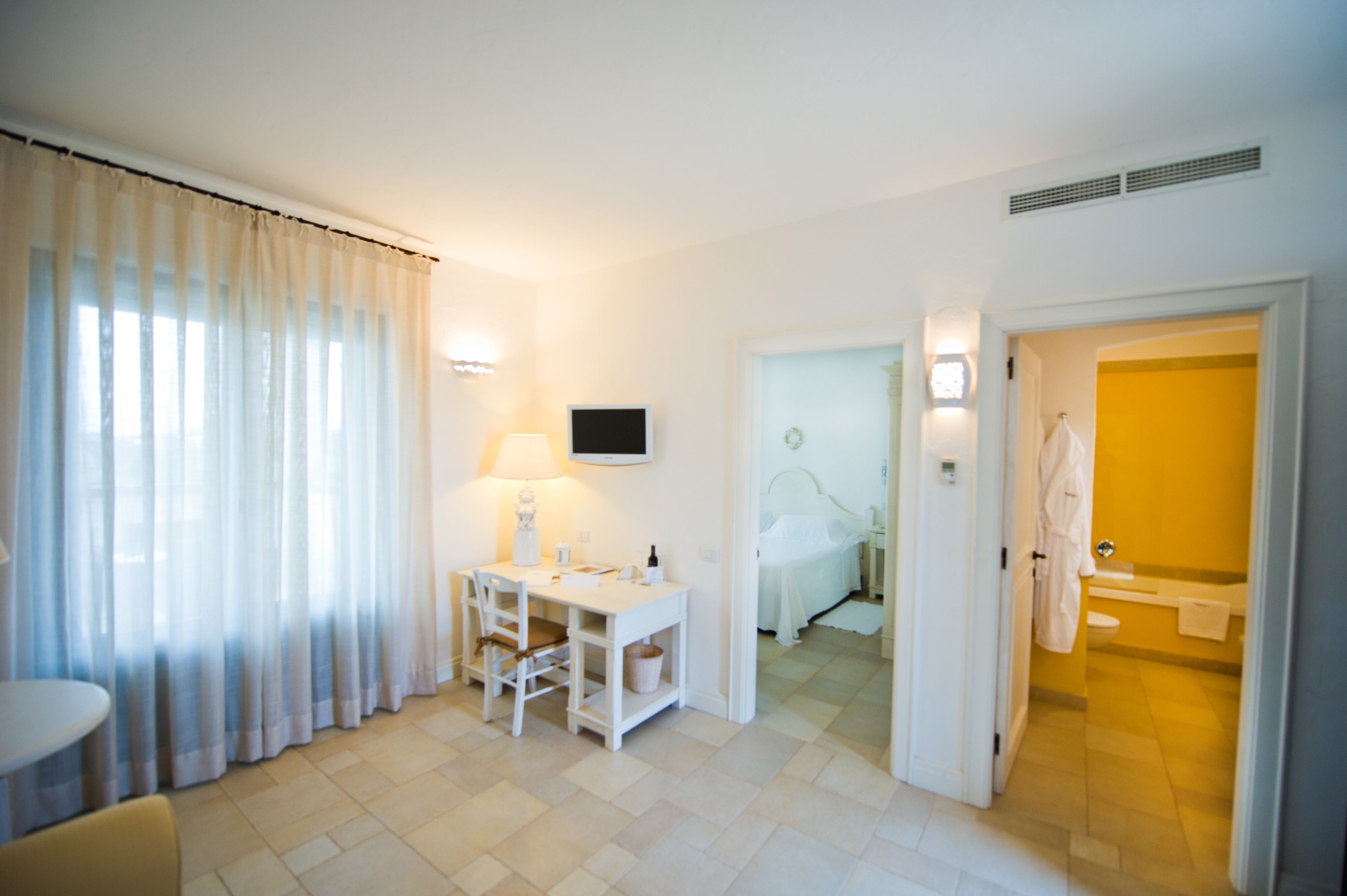 Habitación de hotel con cama, escritorio con silla, televisor y baño con inodoro y lavamanos.