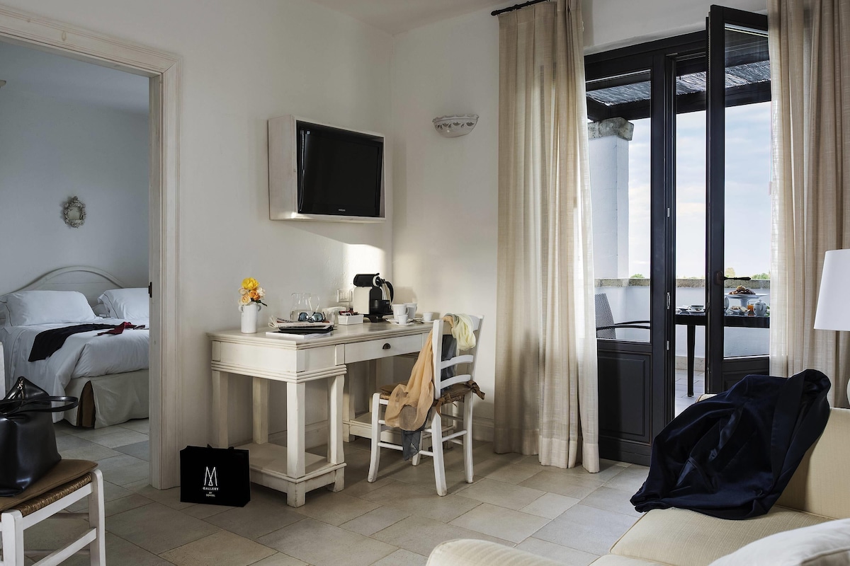 Habitación de hotel con cama, escritorio con computadora, silla, ventana con cortinas y vista al exterior.