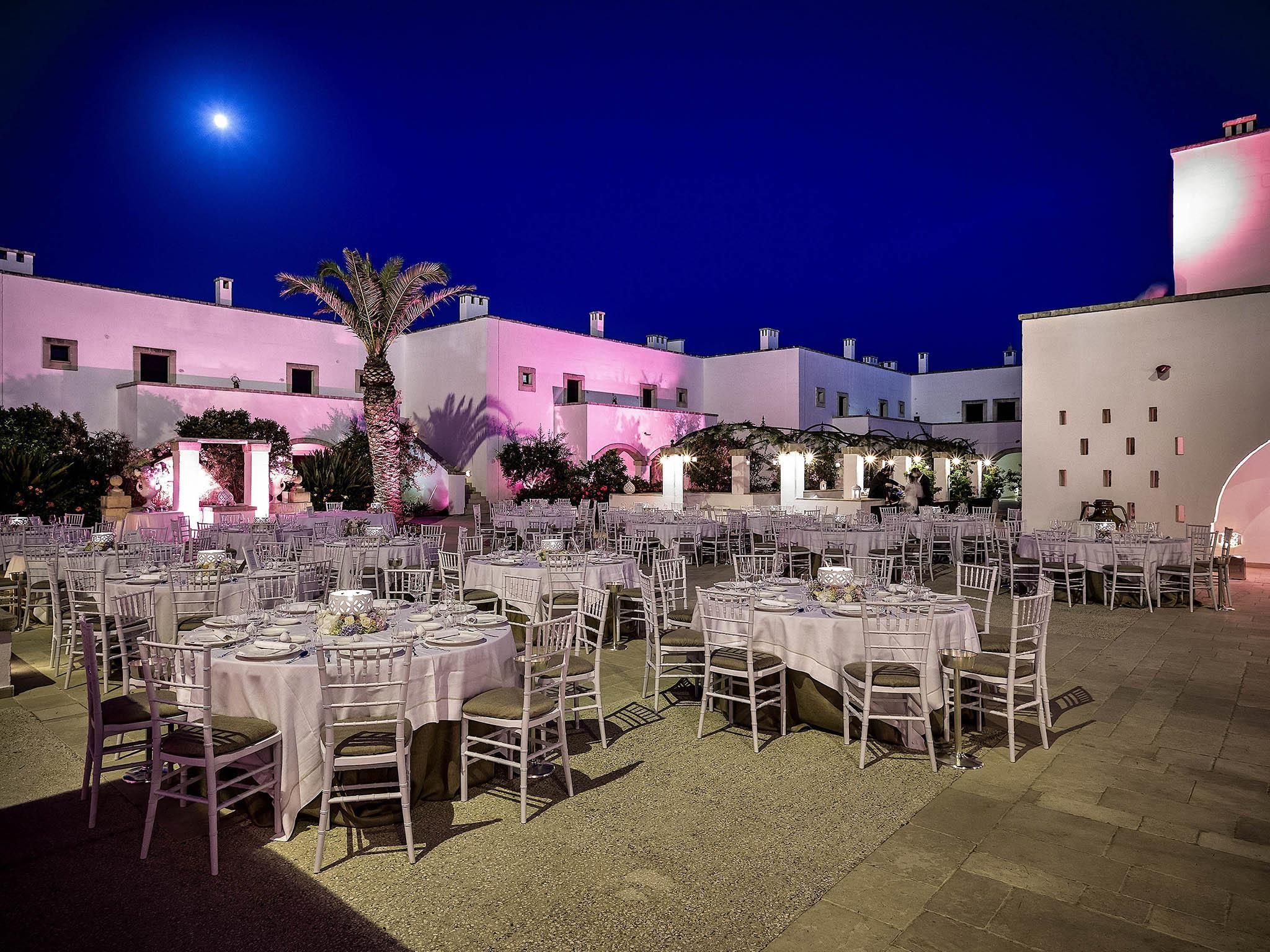 Un espacio exterior con mesas y sillas, una palmera y un edificio al fondo.
