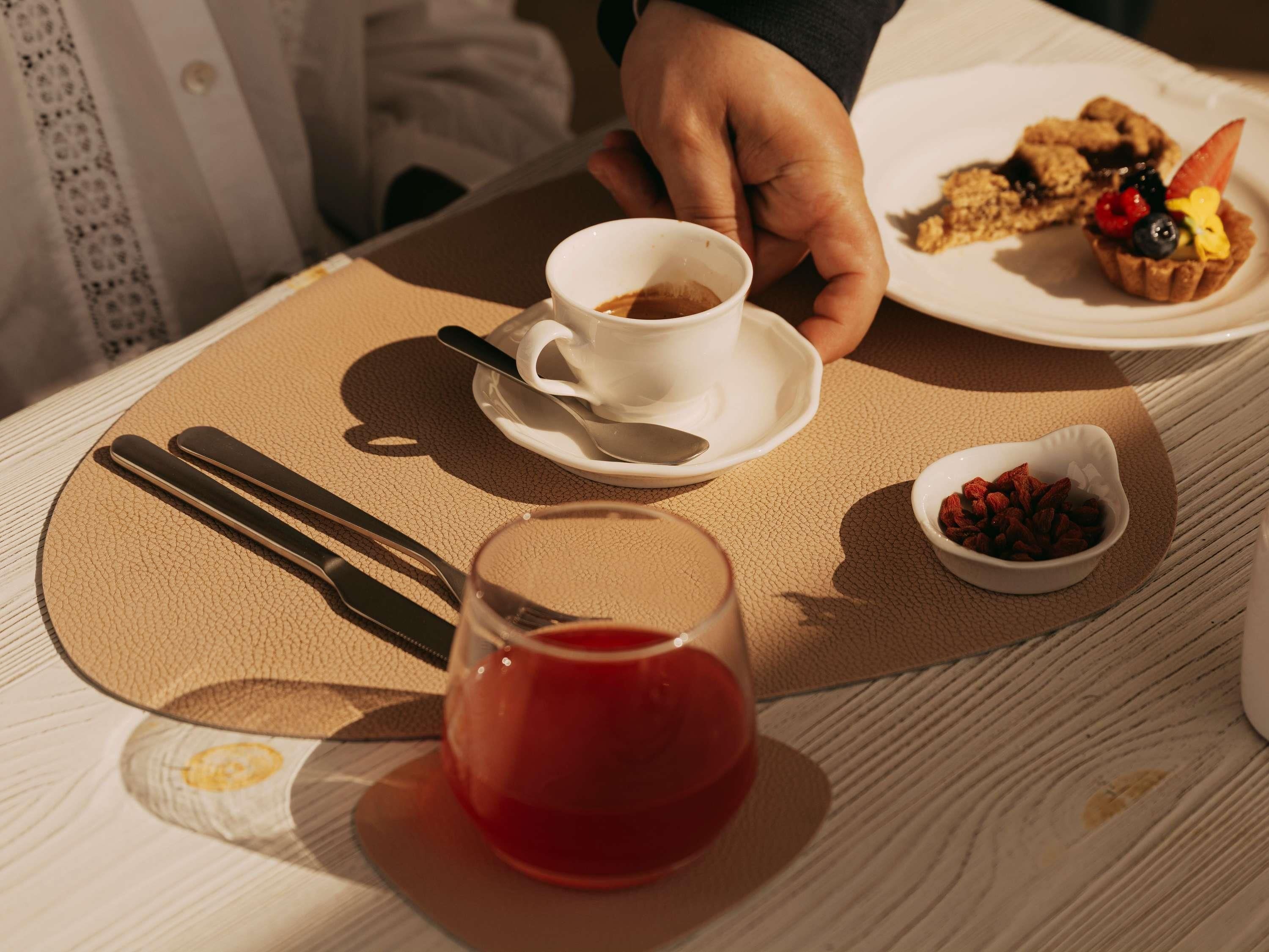 Una mesa con una taza de café, un vaso de bebida roja y un plato con un postre.