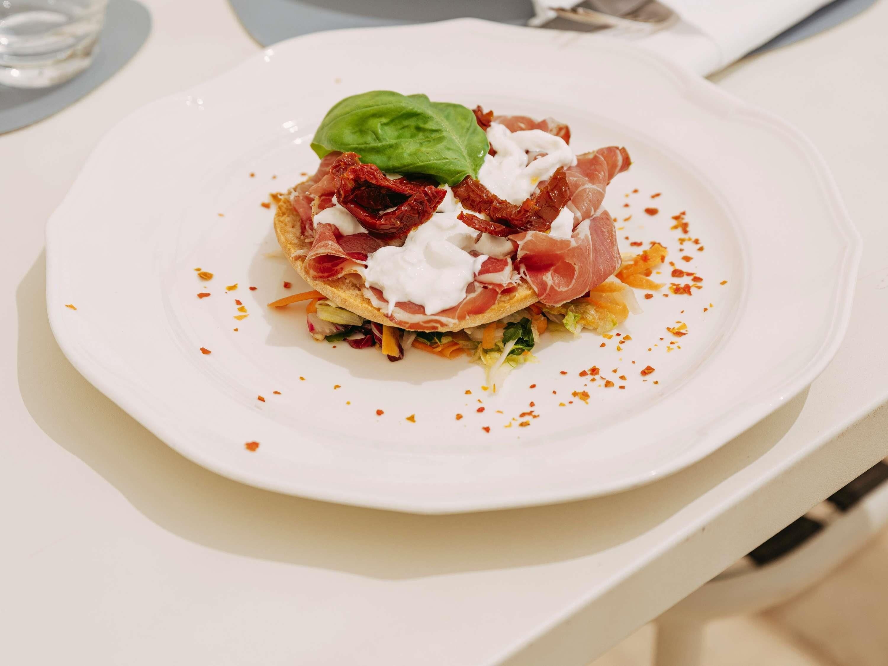 A white plate with a sandwich, a basil leaf, and some red pepper flakes.