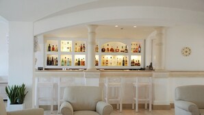 Zona de bar con varias estanterías llenas de botellas, taburetes blancos y una decoración interior en tonos blancos.
