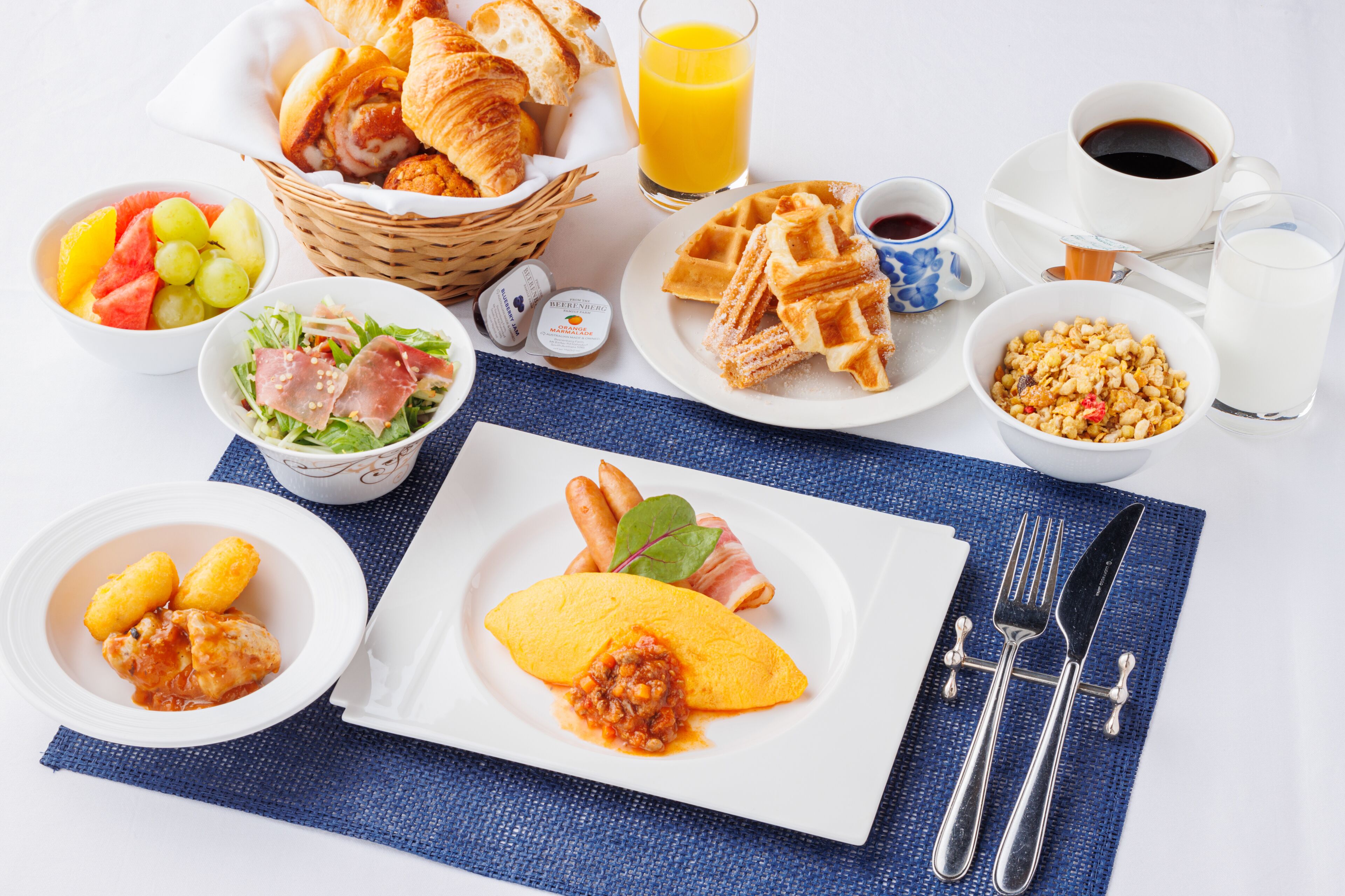 A breakfast table with croissants, waffles, fruit, and various beverages.