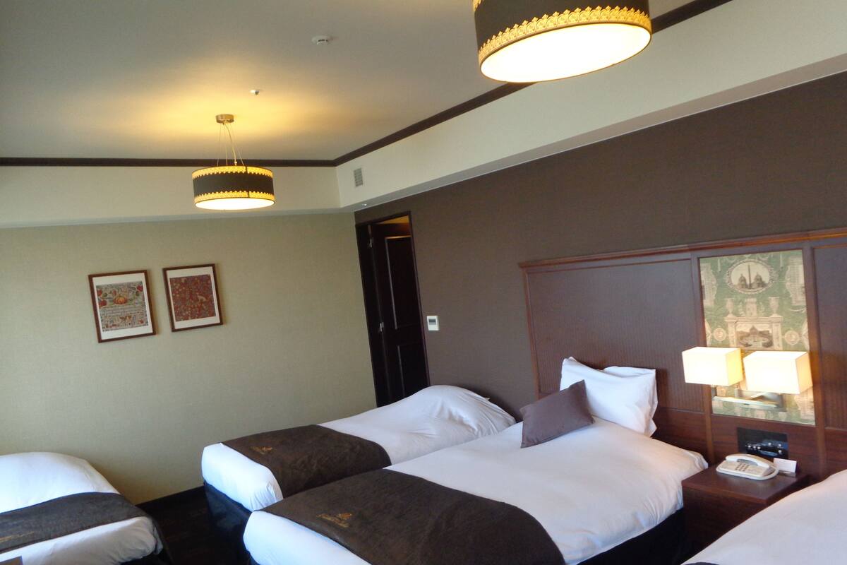 A hotel room with two beds, a nightstand with a lamp, and framed pictures on the wall.