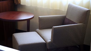 Un sillón a cuadros con un reposapiés a juego, una mesa redonda de madera y una ventana con cortinas de gasa.