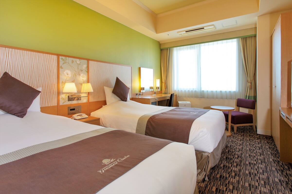 A hotel room with two beds, a desk, a chair, and a small table.