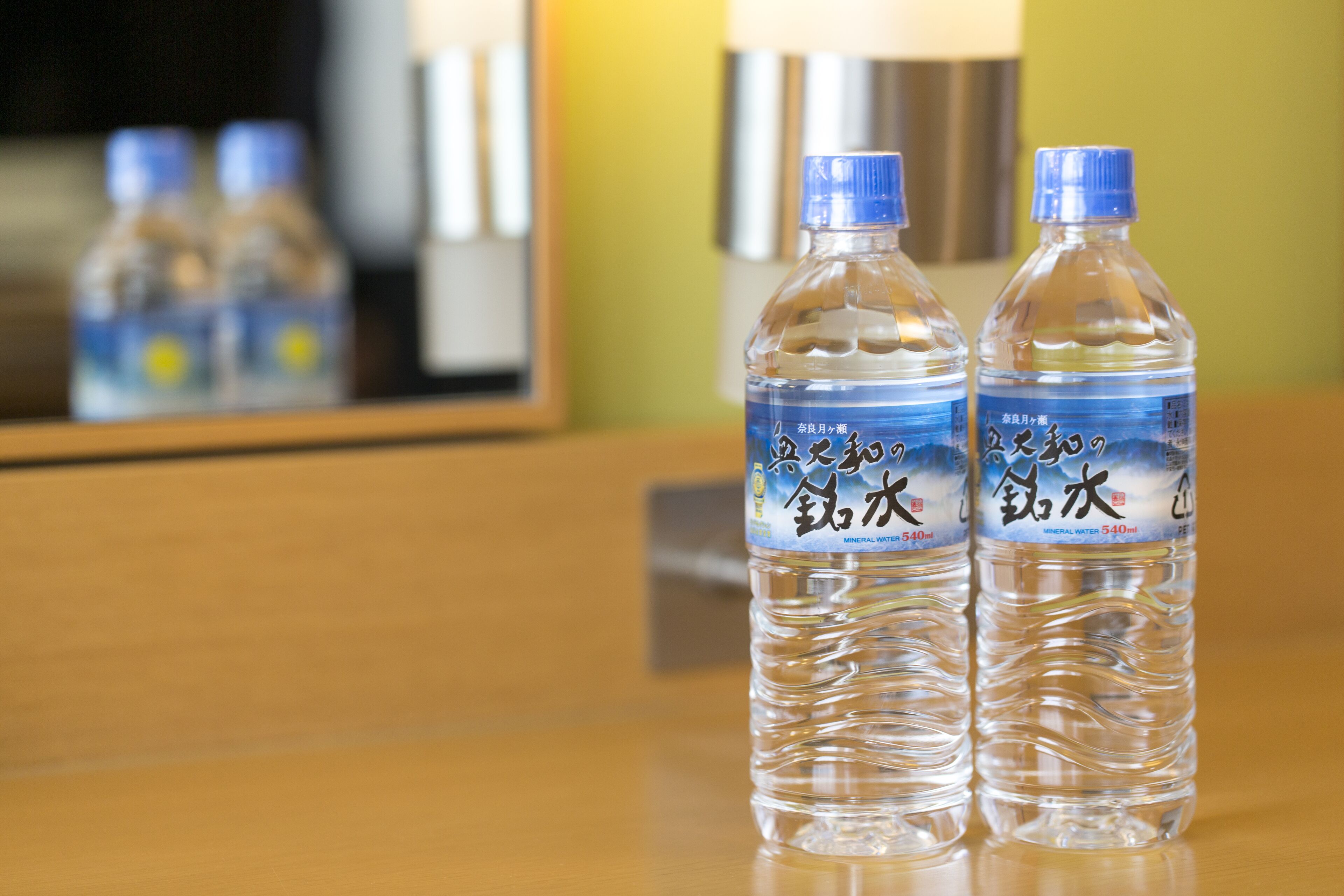 Two mineral water bottles on a wooden surface with a mirror reflecting the bottles and a metallic object in the background.