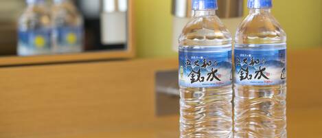 Two mineral water bottles on a wooden surface with a mirror reflecting the bottles and a metallic object in the background.