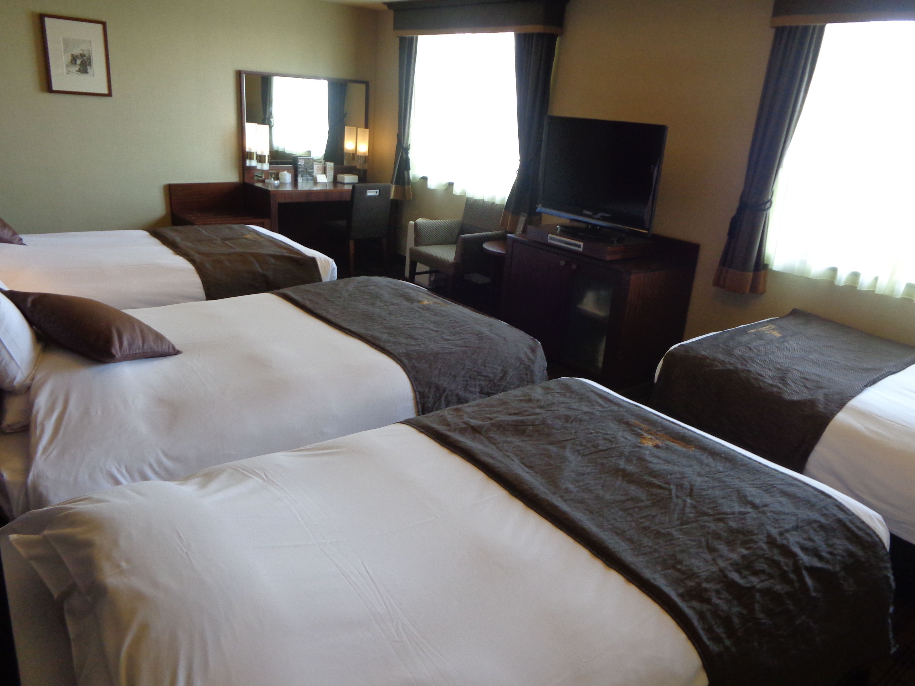 A hotel room with three beds, a desk, a television, and a mirror.