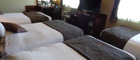A hotel room with three beds, a desk, a television, and a mirror.