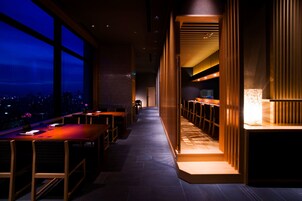 Un restaurante moderno con una barra larga, sillas de madera y vistas de la ciudad por la noche.