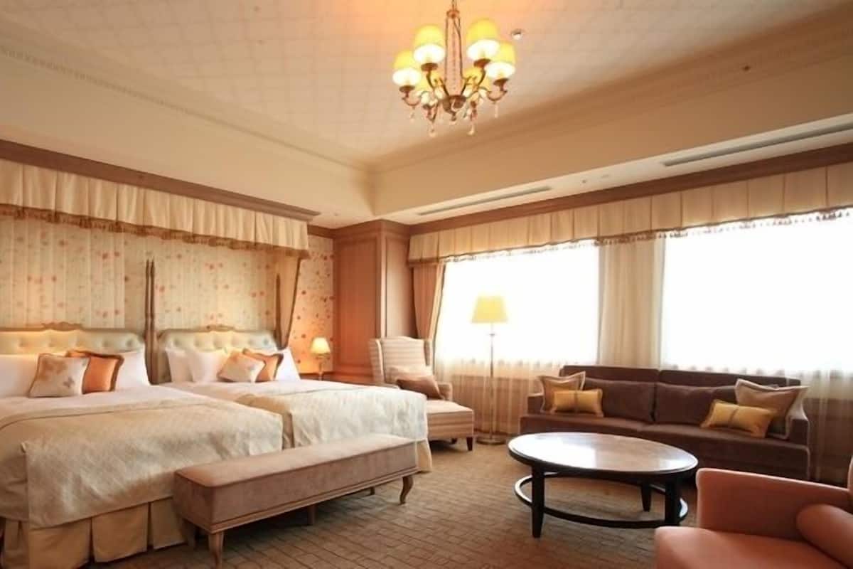A hotel room with two large beds, a sofa, a coffee table, and a chandelier.