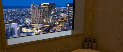 A bathroom with a large window displaying a cityscape at night.