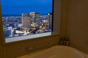 A bathroom with a large window displaying a cityscape at night.