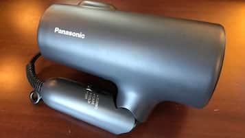 Un secador de pelo Panasonic con cable y un accesorio más pequeño sobre una superficie de madera.