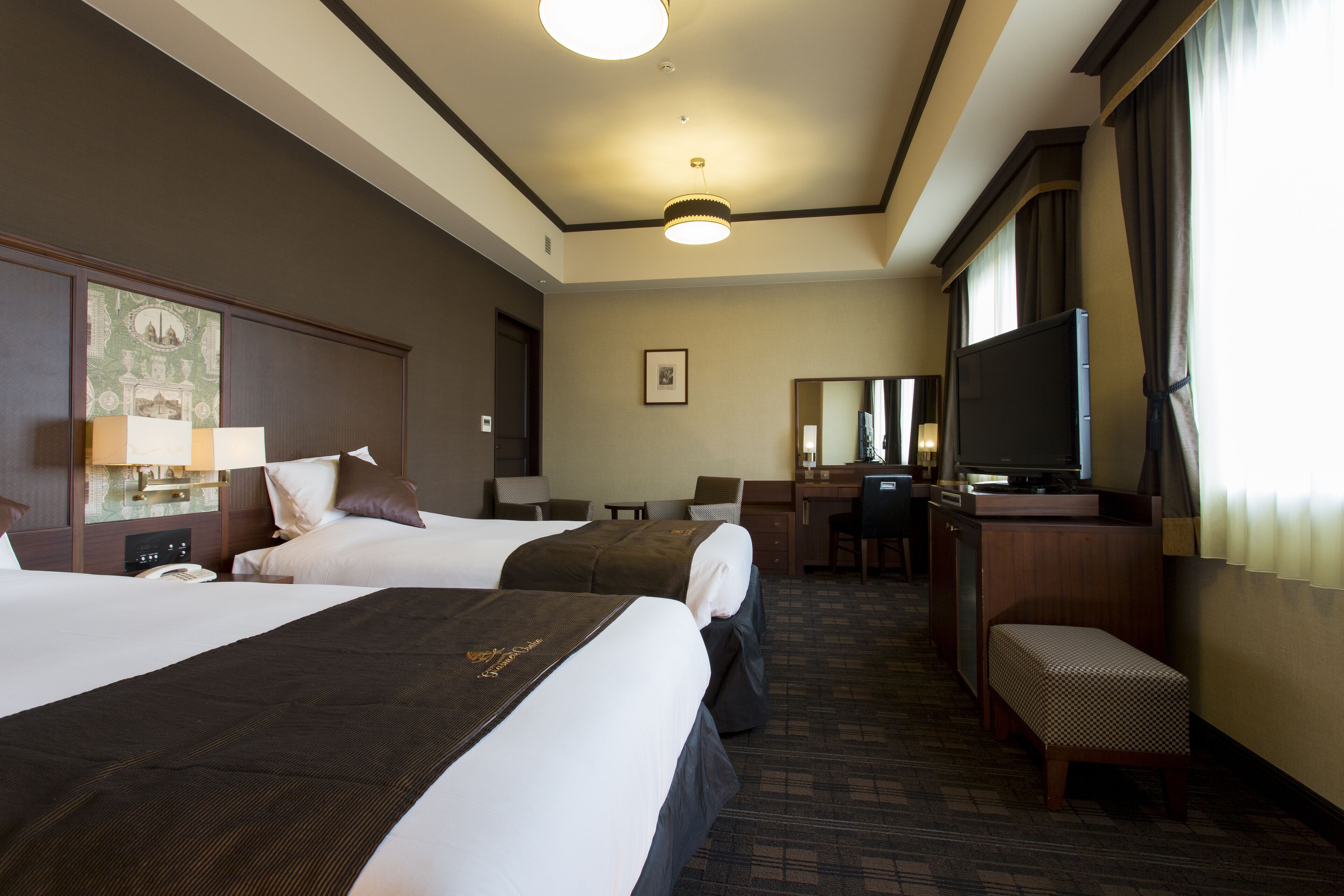 A hotel room with two beds, a desk, a television, and a mirror.