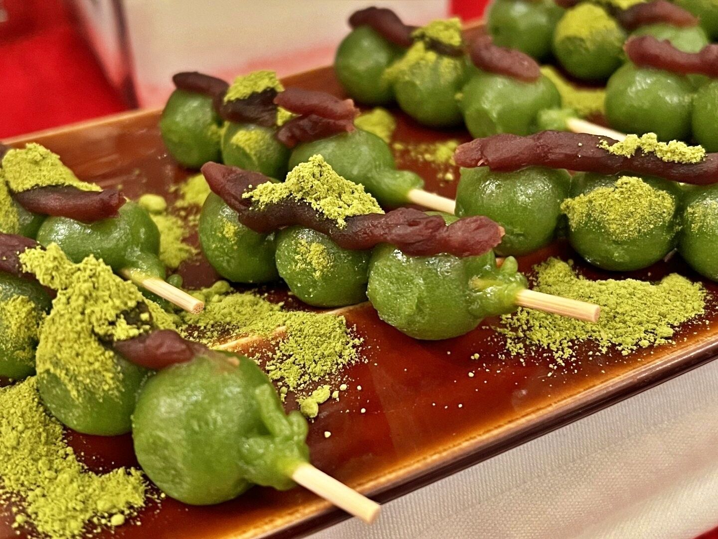 A tray of green fruit skewers with a brownish substance and green powder, possibly a dessert or snack.