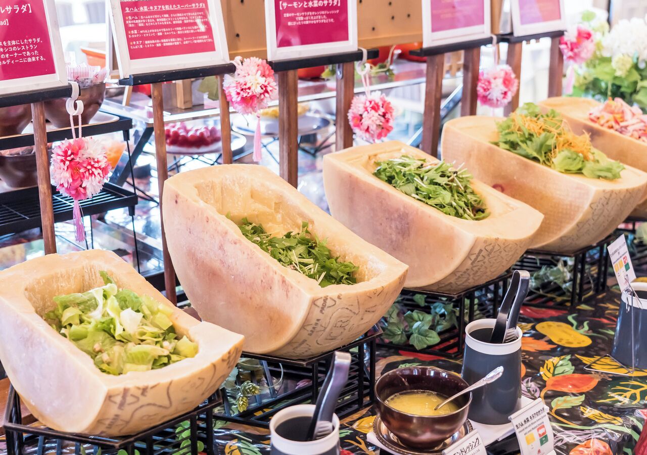 A food display with wooden bowls containing salads and a coffee station with cups and a spoon.
