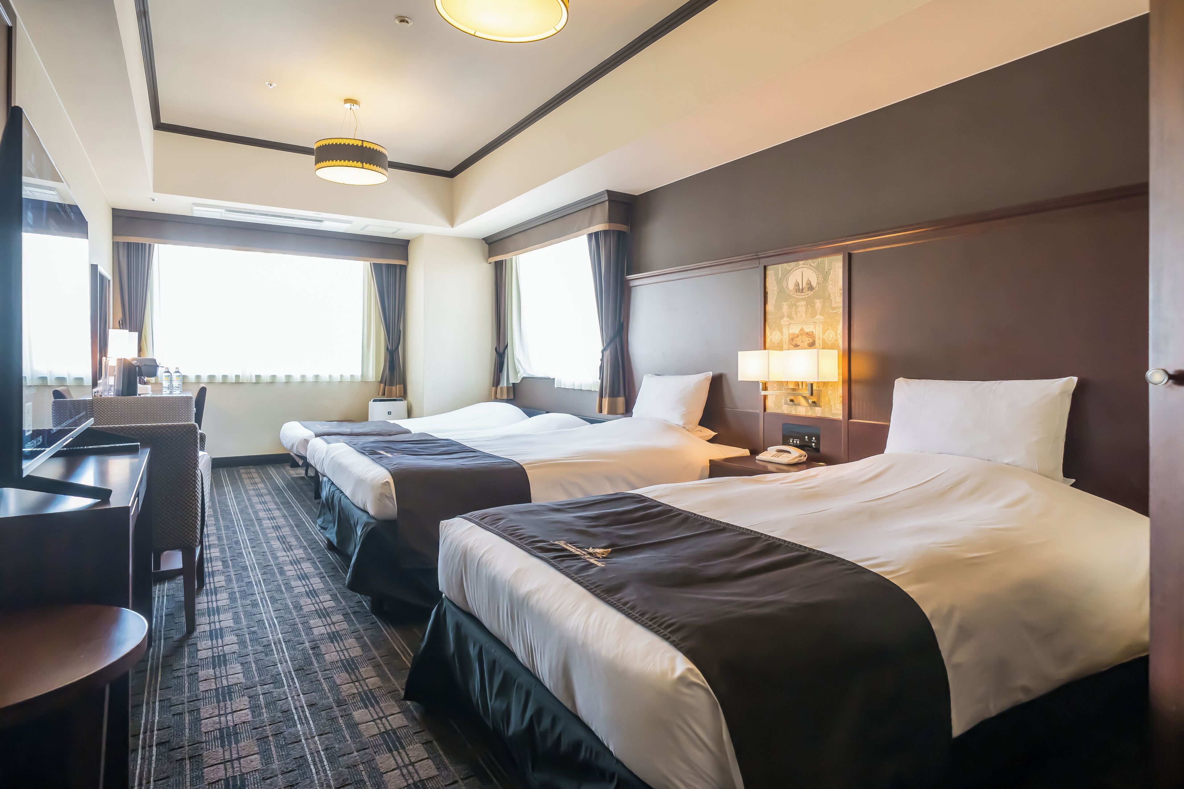Quarto de hotel com duas camas, uma escrivaninha e uma janela grande.