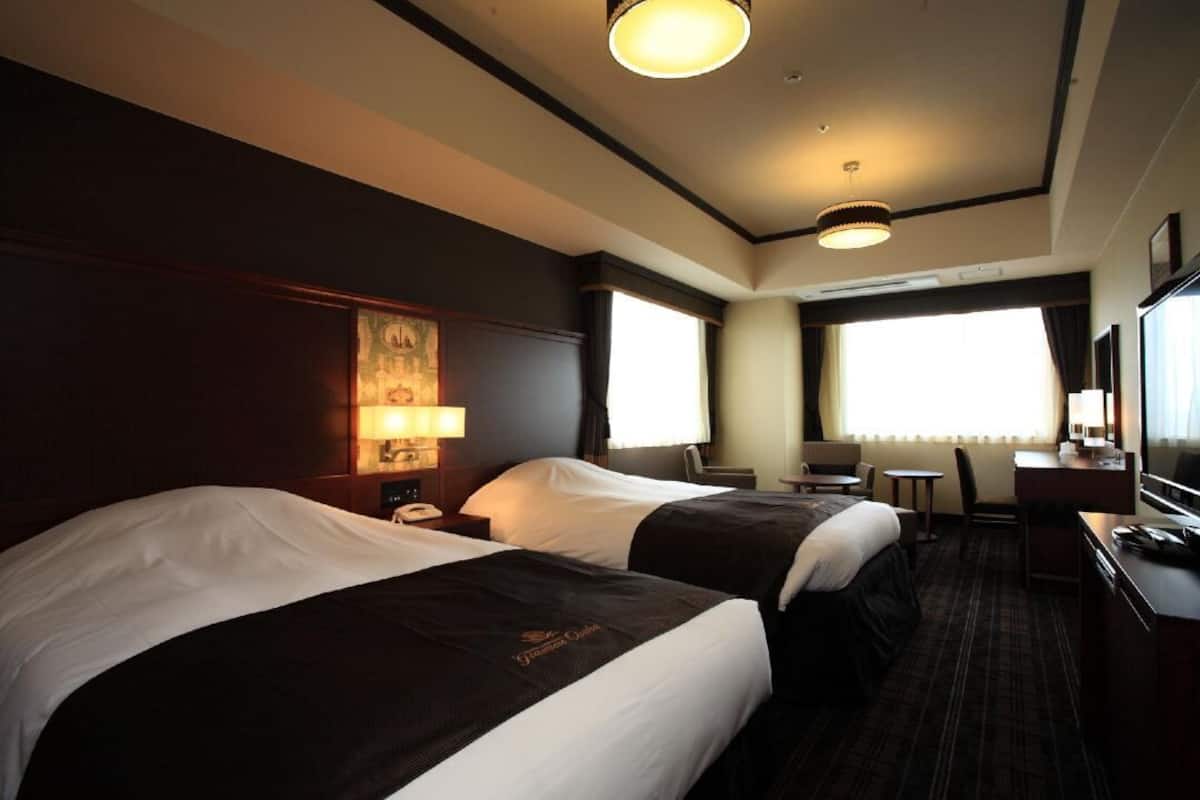 A hotel room with two beds, a desk, a chair, and a television.