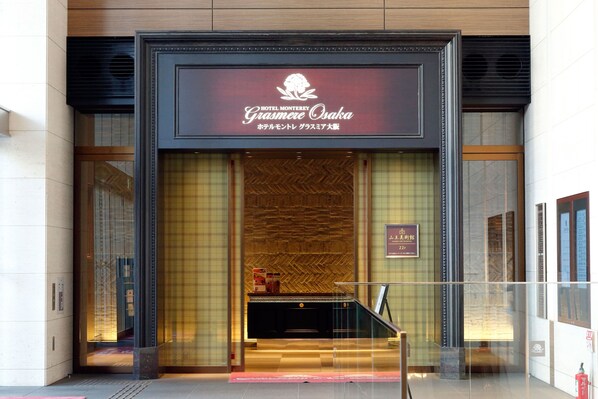 The entrance to Hotel Monterey Gramere Osaka with a modern facade and a sign above the entrance.