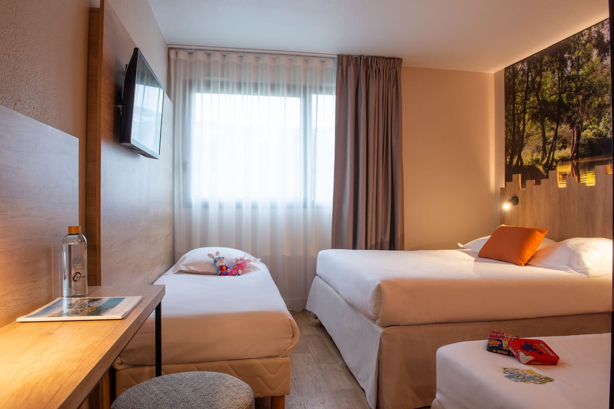 Une chambre d’hôtel avec deux lits, un bureau, un téléviseur fixé au mur et une fenêtre avec des rideaux.