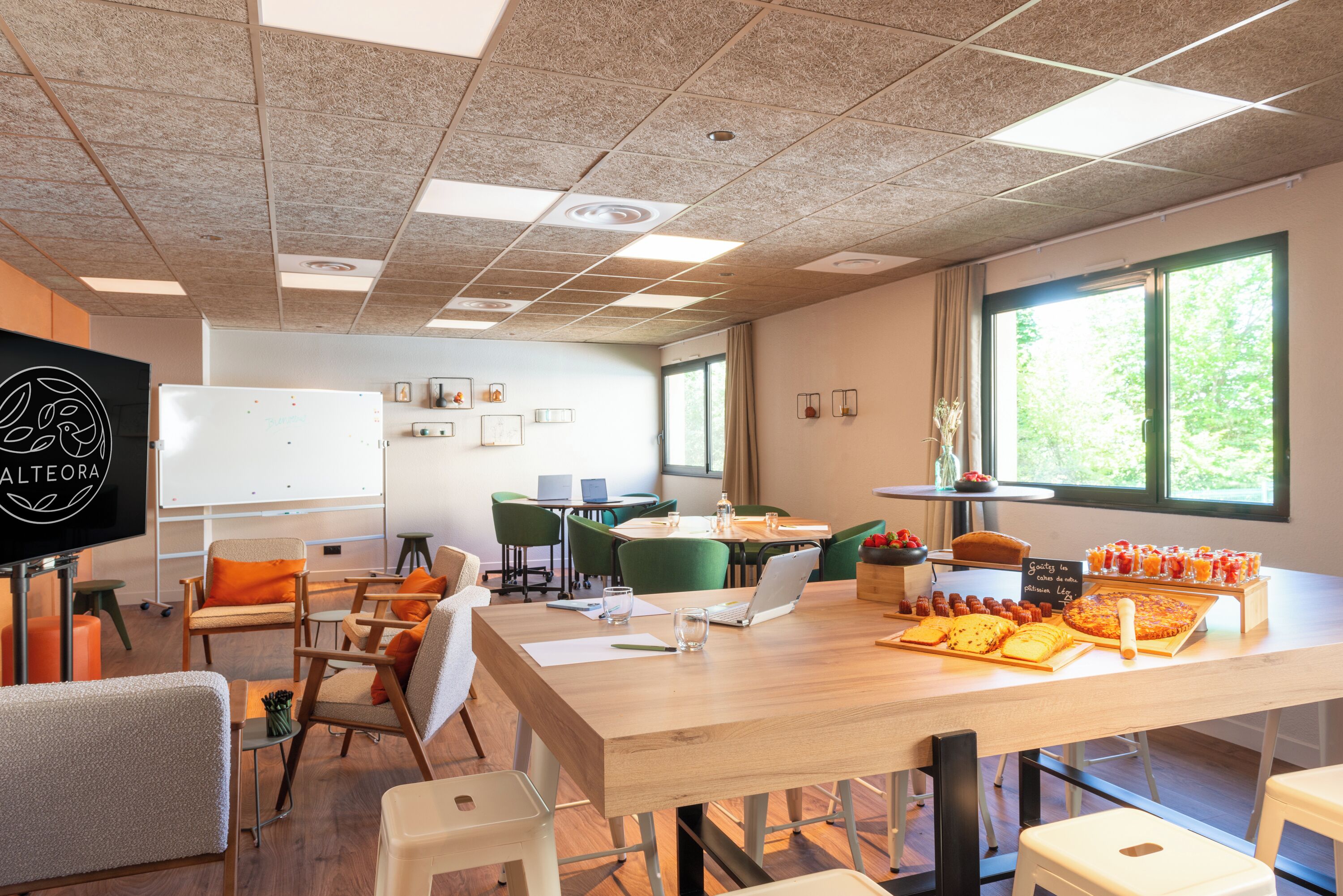 A modern meeting room with a whiteboard, green chairs, a long table with food, and large windows.