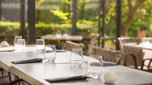 An outdoor dining area with tables set for two, clear glasses, and a white spherical object on the table.
