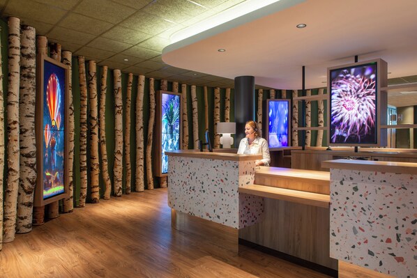 Zona de recepción con decoración de abedules, mostrador de madera y grandes pantallas digitales mostrando patrones florales.