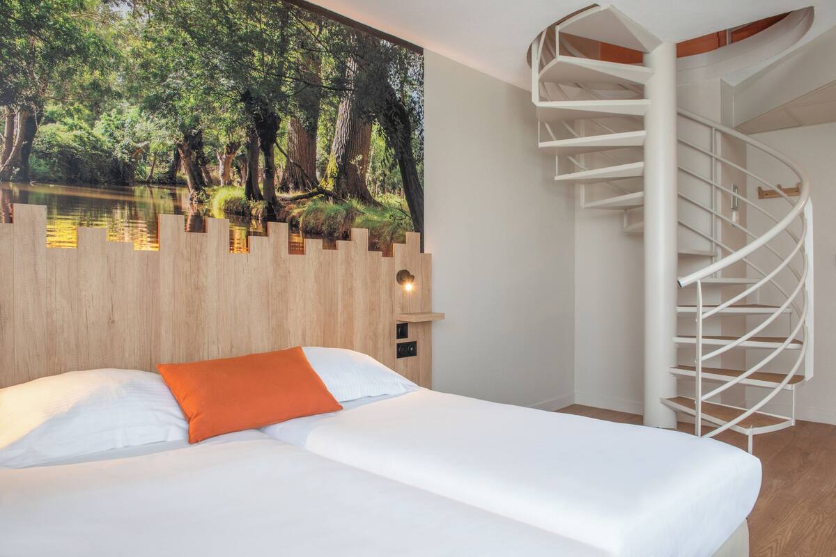 Une chambre avec un lit, un escalier en colimaçon et une grande fresque murale représentant une scène de forêt.