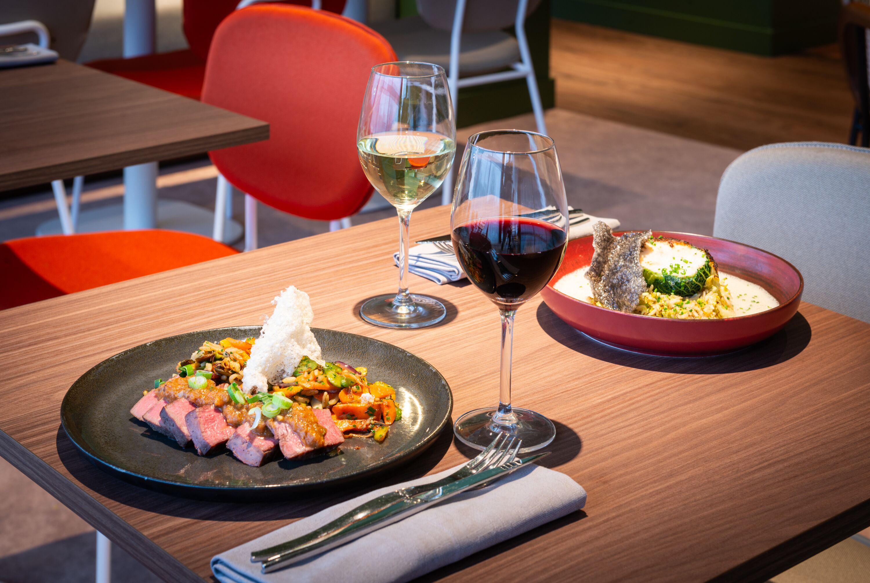 Une table à manger avec deux assiettes de nourriture, deux verres à vin et une fourchette.