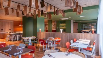 Un restaurante moderno con elementos colgantes de madera, paredes verdes y diferentes opciones de asientos, incluyendo mesas y sillas.
