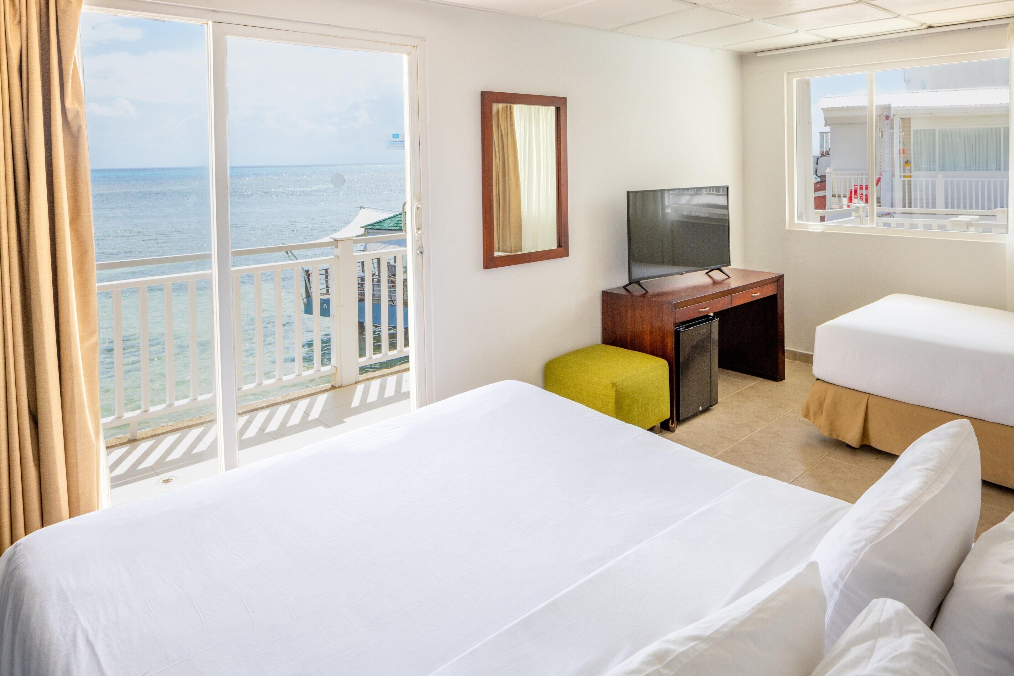 A hotel room with a balcony, a bed, a desk, a television, and a window with a view of the sea.