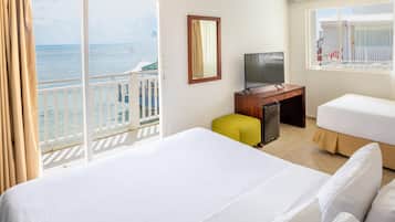 A hotel room with a balcony, a bed, a desk, a television, and a window with a view of the sea.