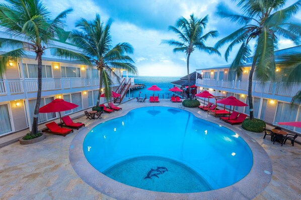 A swimming pool with red lounge chairs and umbrellas, surrounded by palm trees and hotel buildings. - Decameron Los Delfines All Inclusive (San Andrés)