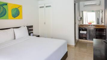 Une chambre d’hôtel avec un lit, une salle de bain dotée d’un lavabo et d’un miroir, et un mur orné d’une peinture représentant des fruits.